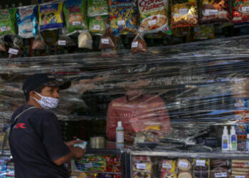 A man shops at a store covered with plastic as a precautionary measure against the spread of the new coronavirus, COVID-19, in Caracas, on March 17, 2020 - President Nicolas Maduro asked the International Monetary Fund on Tuesday for a $5 billion loan to help crisis-worn Venezuela cope with the onslaught of the coronavirus. (Photo by Cristian Hernandez / AFP)