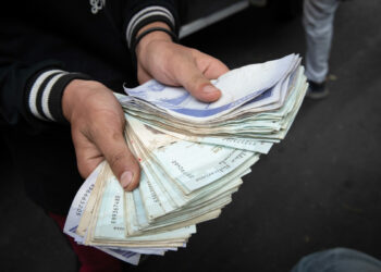 AME7281. CARACAS (VENEZUELA), 30/03/2023.- Un trabajador del transporte público muestra hoy un fajo de bolívares, en Caracas (Venezuela). El salario mínimo en Venezuela, que ha aumentado desde hace un año de 7 bolívares (1,60 dólares) a 130 bolívares (29,68 dólares), se ha reducido desde entonces un 82 % en su equivalente en la divisa estadounidense -referencia en el país para fijar precios- hasta 5,31 dólares, como consecuencia de la devaluación de la moneda local. EFE/ Rayner Peña R