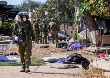 Israeli soldiers stand near the body of a Palestinian militant in Kfar Aza, in the south of Israel, bordering Gaza Strip on October 10, 2023. Israel pounded Hamas targets in Gaza on October 10 and said the bodies of 1,500 Islamist militants were found in southern towns recaptured by the army in gruelling battles near the Palestinian enclave. (Photo by Thomas COEX / AFP)